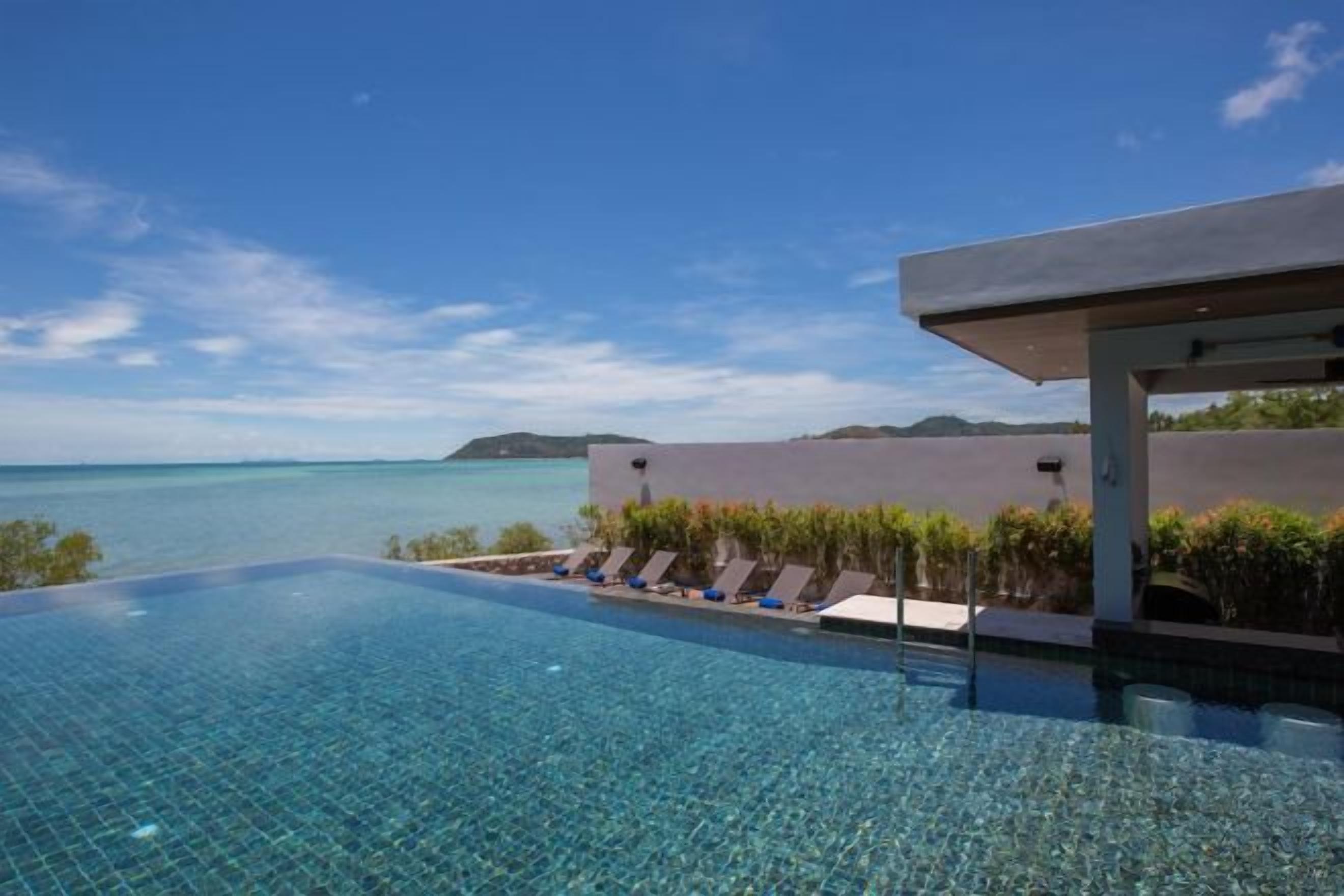 An infinity pool with a clear view of the sea, lounge chairs, and a modern building structure.