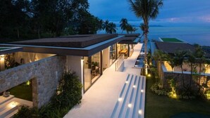 A modern house with a glass facade, outdoor seating, and a view of the ocean. - Exclusive Sea Renity A Beachfront Villa Retreat Sleeps 12 Adults and 6 Kids (Koh Samui)