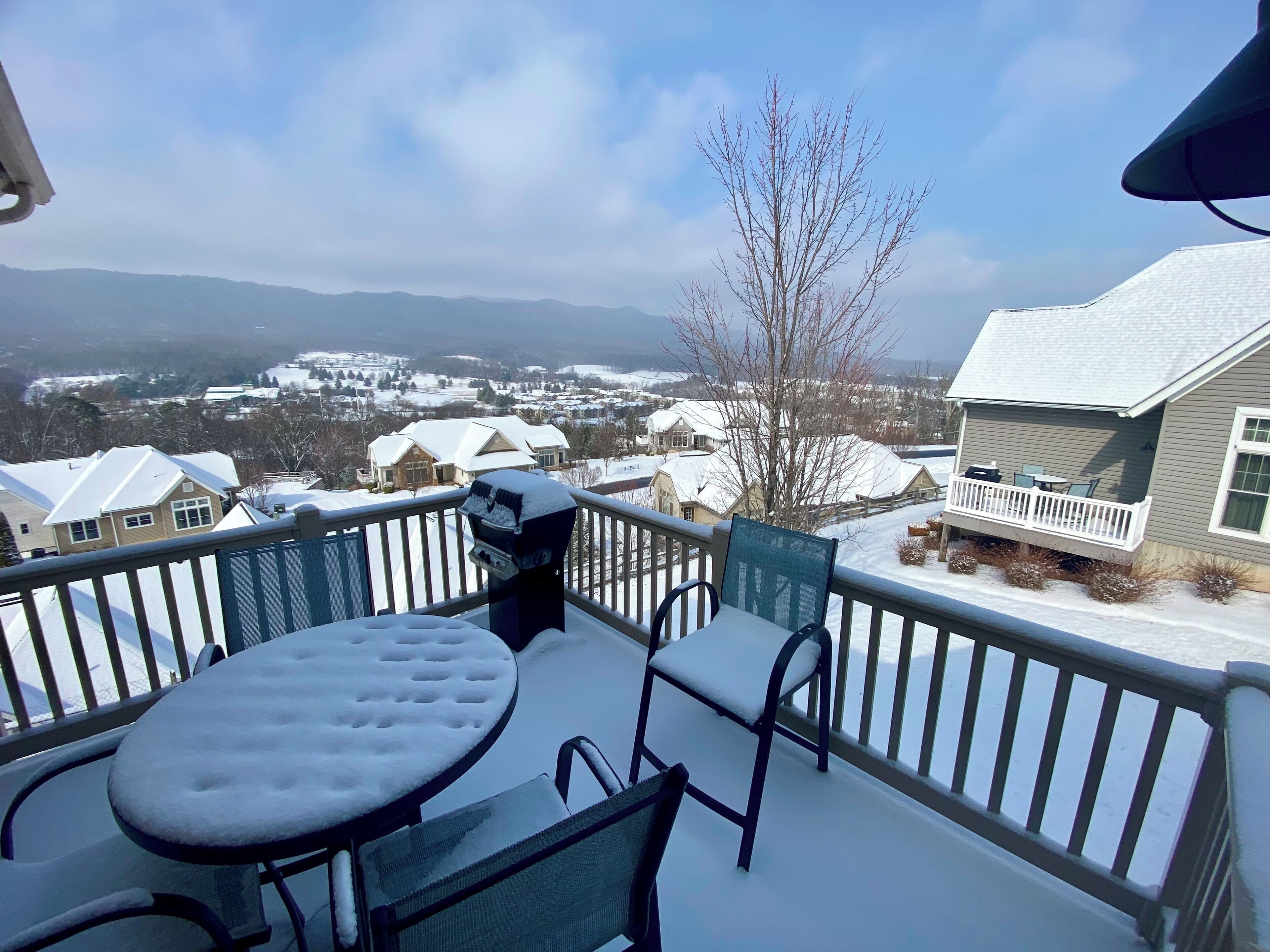 Ein Balkon mit Tisch und Stühlen, einem Grill und Blick auf eine verschneite Landschaft mit Häusern und Bergen in der Ferne.