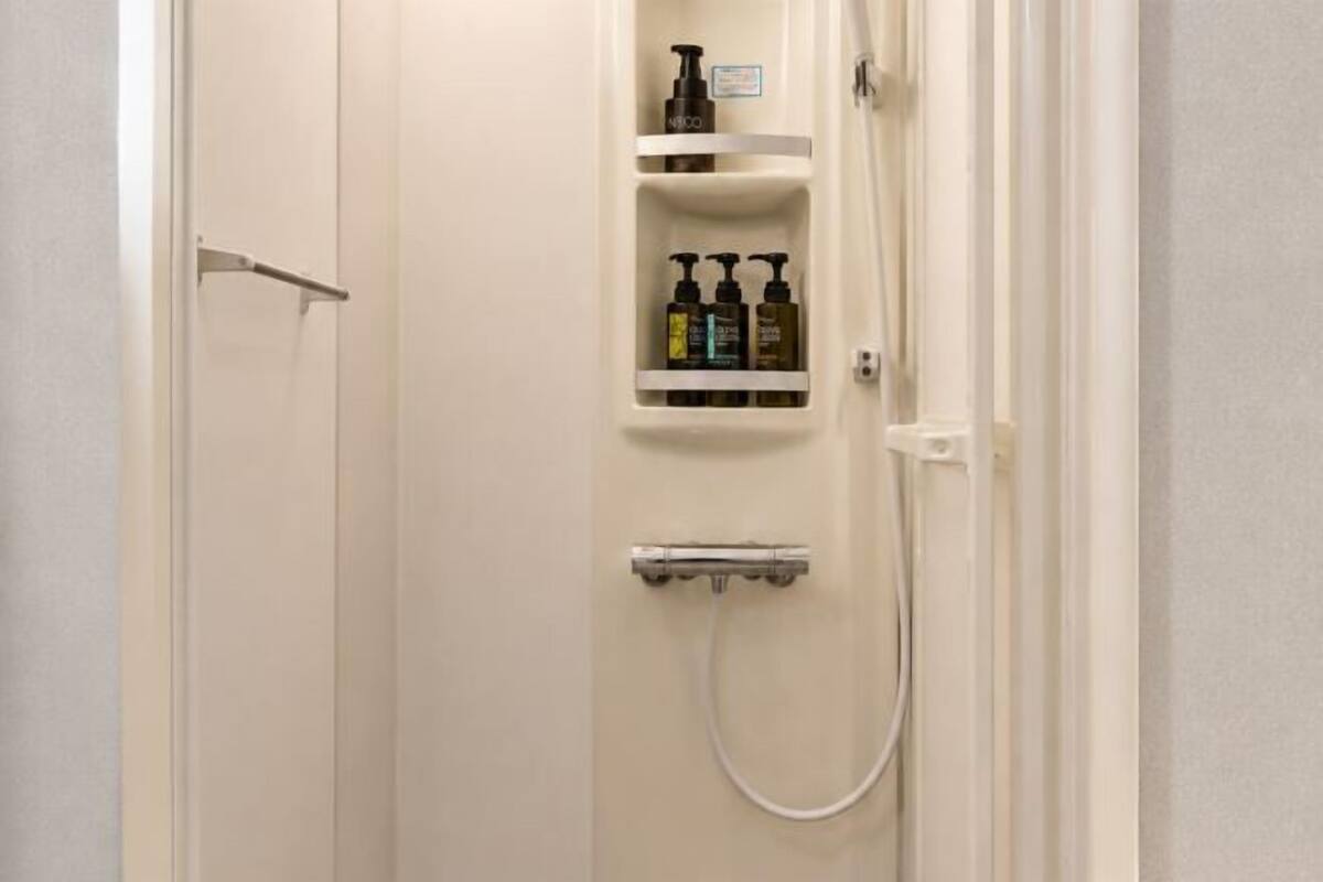 A bathroom with a shower, a shelf with toiletries, and a towel rack.