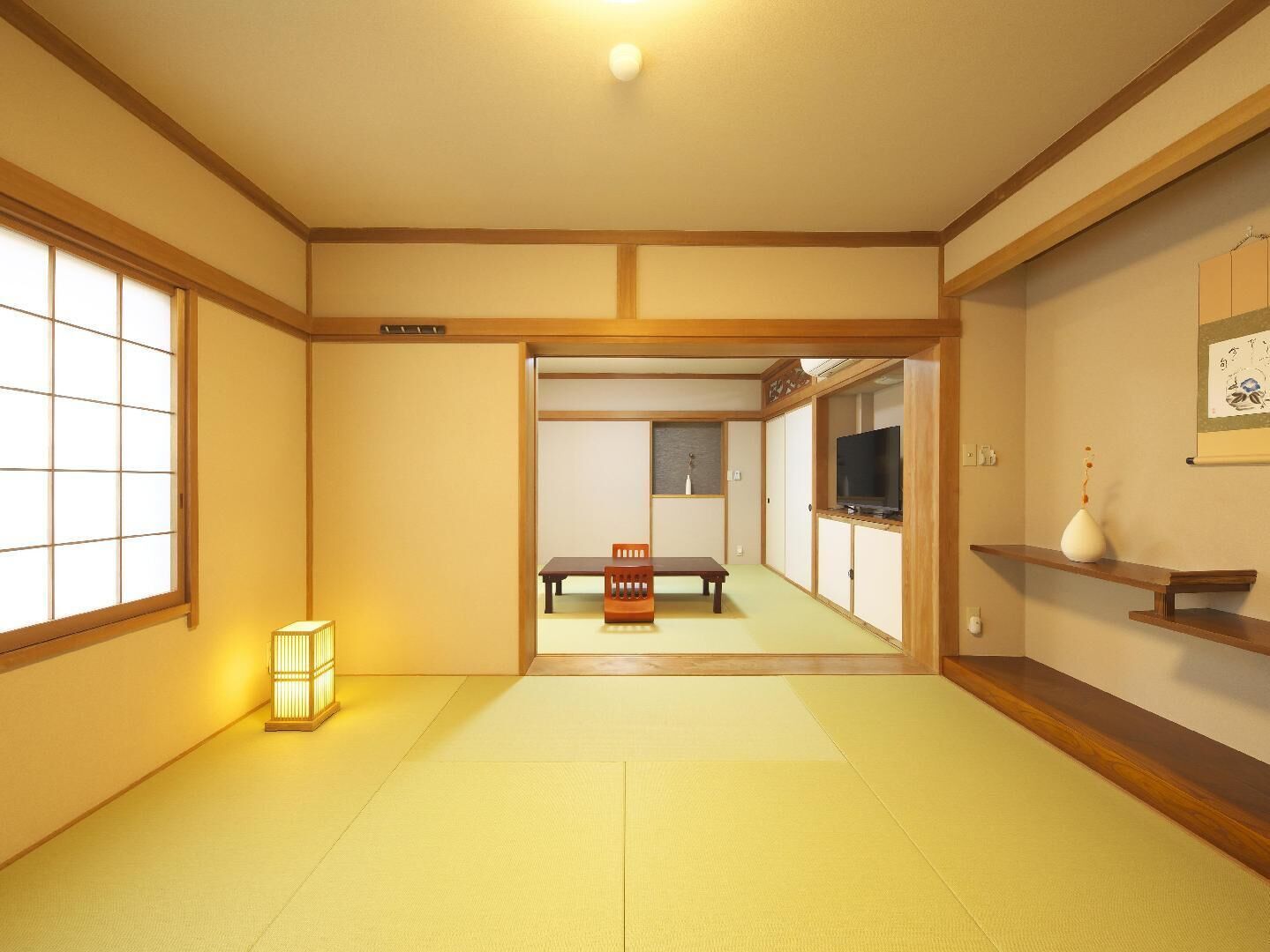 A traditional Japanese room with tatami flooring, a low table with a chair, a television, and a shelf with a vase.