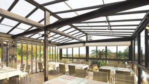 A covered outdoor dining area with glass tables and wicker chairs, large windows, and a view of the surrounding landscape. - Ito Villa-TOKI- (Ito)