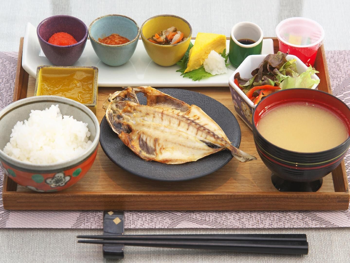 A tray with a whole grilled fish, rice, soup, and various side dishes.