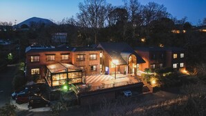 A multi-story building with a covered patio, a carport, and a mountain in the background. - Ito Villa-TOKI- (Ito)