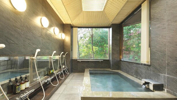 A modern spa room with a large bathtub, multiple showerheads, and a large window offering a view of greenery. - Ito Villa-TOKI- (Ito)