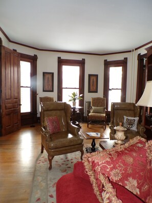 A room with two leather armchairs, a red sofa, and a wooden floor. - The Trillium House at DePauw - 4/5 BR 3.5 BA (Greencastle)