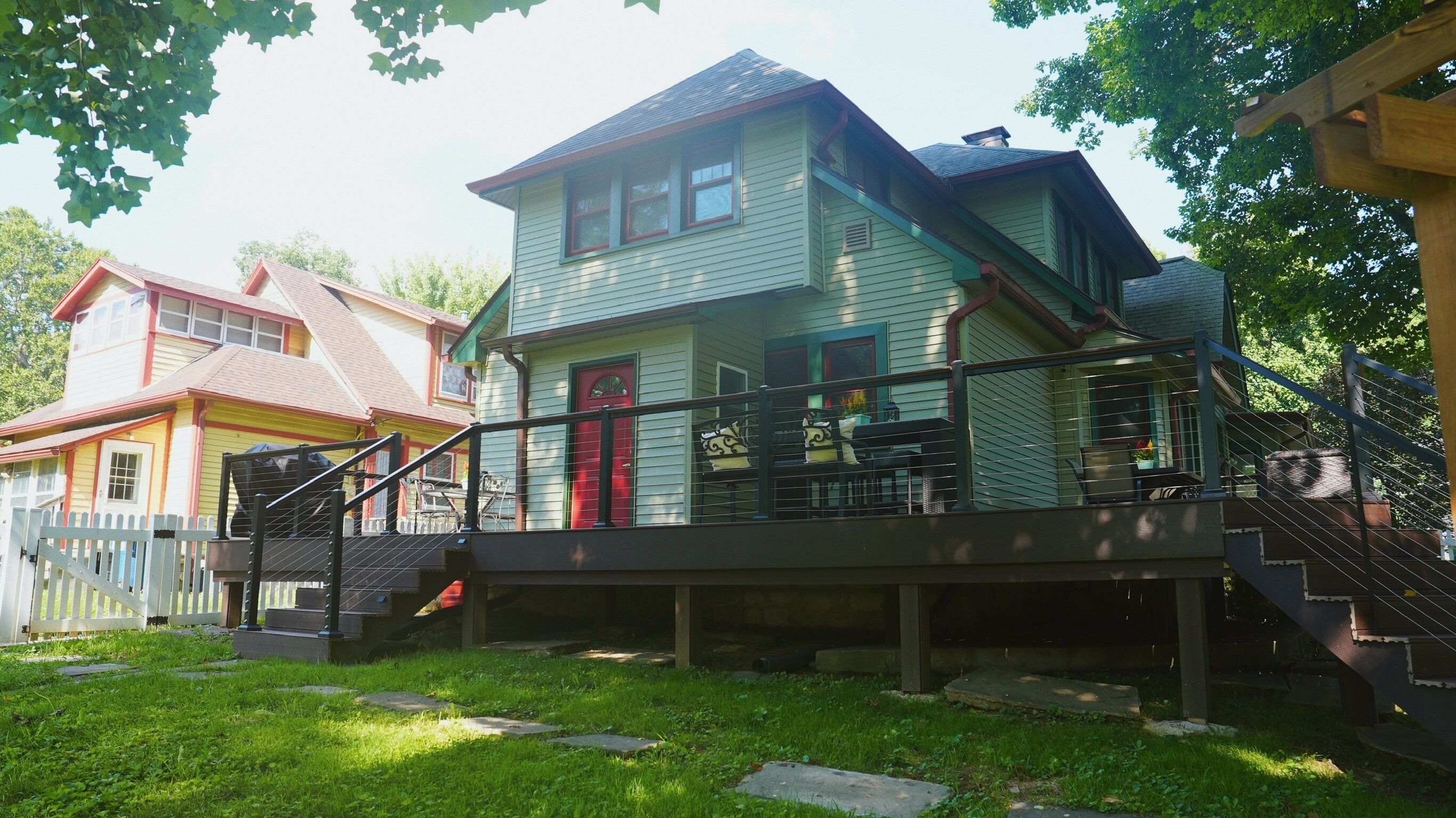 A two-story house with a porch, a red door, and a staircase leading to the upper level.