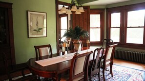 A dining room with a wooden table, chairs, a vase with a plant, and a framed botanical illustration on the wall. - The Trillium House at DePauw - 4/5 BR 3.5 BA (Greencastle)
