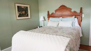 Ein Schlafzimmer mit einem hölzernen Kopfende, einem Bett mit floralem Überwurf, zwei Nachttischlampen und einem gerahmten Bild an der Wand.