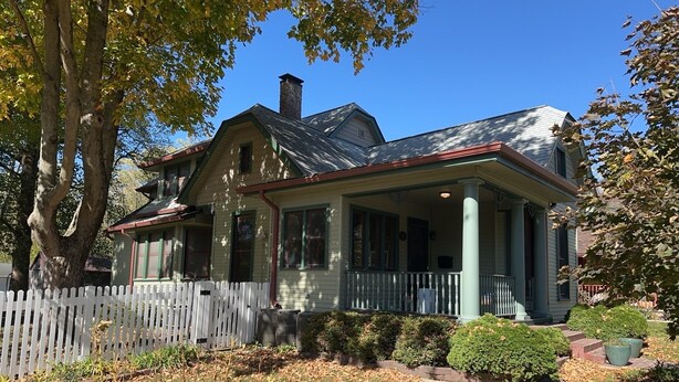 A two-story house with a porch, a chimney, and a white picket fence. - The Trillium House at DePauw - 4/5 BR 3.5 BA (Greencastle)