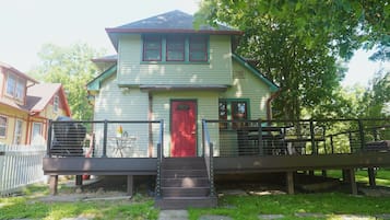 A two-story house with a red door, a front porch with a railing, and a small outdoor seating area.