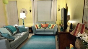 Un salon avec un canapé gris, un canapé bleu, un tapis bleu et une table d’appoint en bois agrémentée d’objets décoratifs.