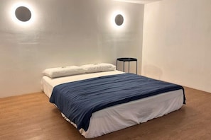 Un dormitorio con una cama, dos luces fijadas a la pared y una mesita de noche pequeña.