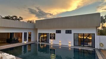 A modern house with a swimming pool, large windows, and a well-lit interior.