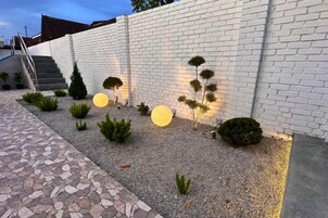 Un jardín ajardinado con muro de ladrillo blanco, suelo de grava y diversas arbustos y árboles.