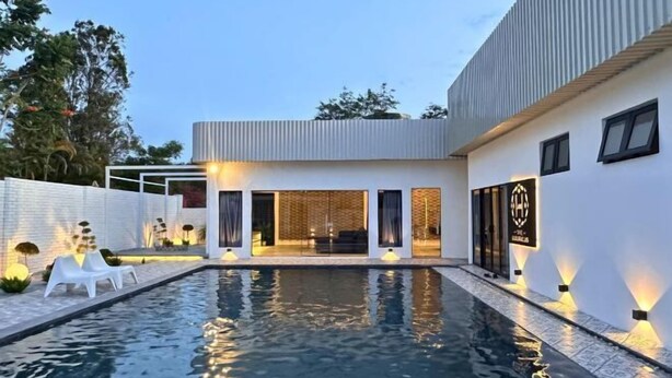 Una casa moderna con piscina, mobiliario exterior y una entrada bien iluminada.