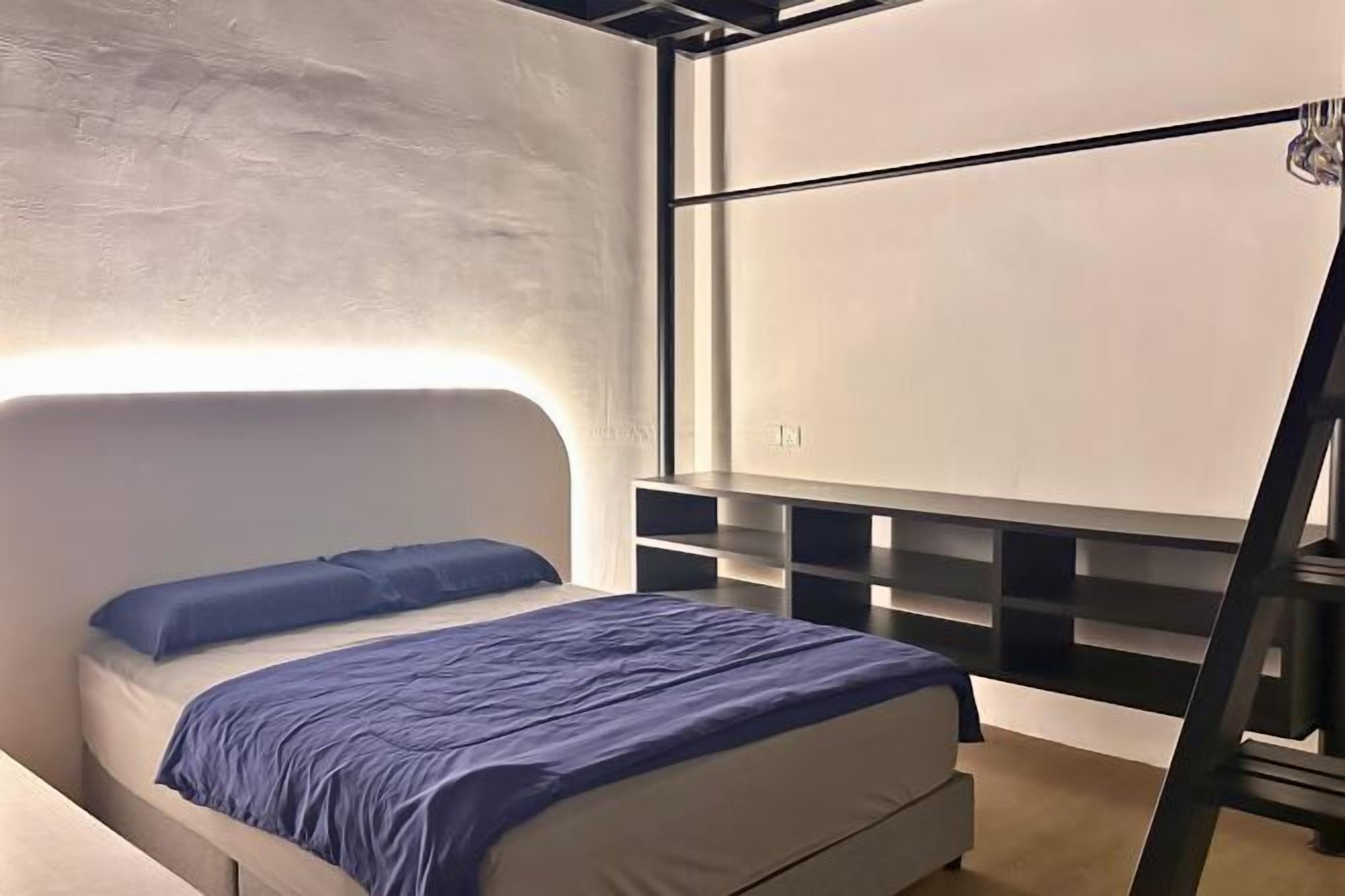 A modern bedroom with a bed, a headboard, a wall-mounted shelf unit, and a ladder.