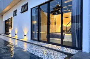 A modern hotel room with a large sliding glass door, a bed, and a visible bathroom.