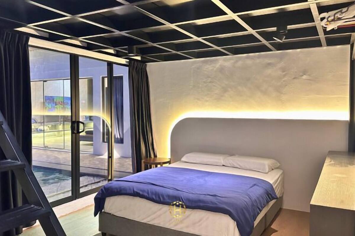 A modern hotel room with a bed, a desk, and a view of a pool and outdoor area.