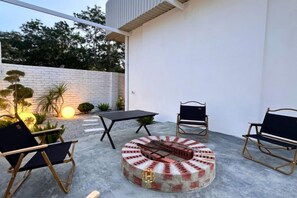 An outdoor patio with a round fire pit, two chairs, a table, and a brick wall. - The Luxurious 1256, Forest Flow Villa (Pegoh)