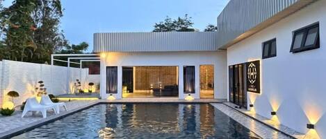 Une maison moderne dotée d’une piscine, d’un espace extérieur aménagé et couvert, et d’un éclairage extérieur soigné.