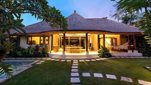 Un resort tropical con un edificio de techo de paja, piscina y césped bien cuidado.