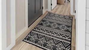 Un couloir avec une porte grise, un panneau d’accueil, un tapis à motifs et un bureau avec une chaise au fond.