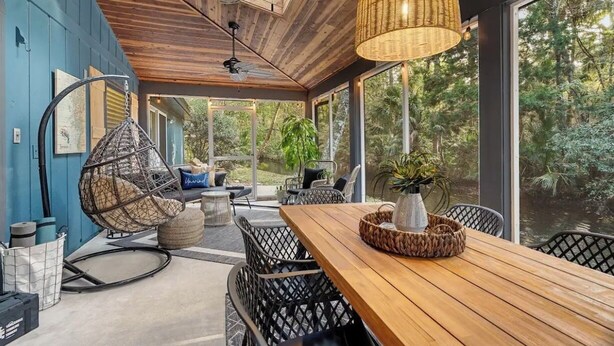 Un espace extérieur aménagé avec une zone salon couverte, comprenant une table en bois, des chaises en osier et un luminaire suspendu.