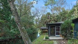 Un cadre paisible au bord de la rivière, avec une maison moderne dotée d’une porte vitrée et d’un chemin en pierre.