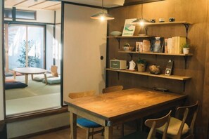 A wooden dining table with chairs, a glass partition, and shelves with books and decorative items.