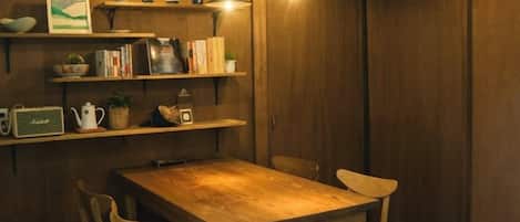 A wooden dining table with chairs, a shelf with books and decorative items, and pendant lights.
