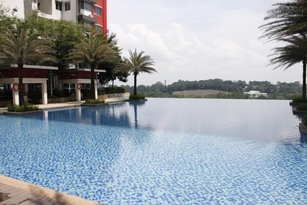 Una piscina con borda piastrellata, circondata da palme e un edificio con facciata rossa.