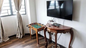 Een kamer met een tafelvoetbaltafel, een aan de muur bevestigde televisie en een tafel met elektronische apparaten.
