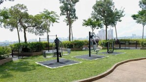 Een buitentrainingsruimte met fitnessapparatuur, banken en uitzicht op een stadshemelbeeld.