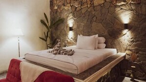 A bed with white linens, a stone wall, and two wall-mounted lights. - Villa Kamar Tamu Selomartani (Kalasan)