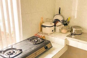 Una cocina con estufa a gas, cocedor de arroz y diferentes utensilios de cocina.