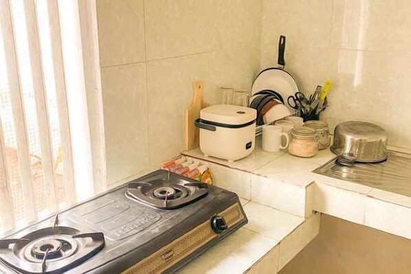 A kitchen with a gas stove, a rice cooker, and various kitchen utensils. - Villa Kamar Tamu Selomartani (Kalasan)