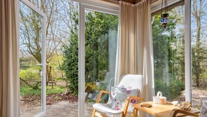 A room with a glass door leading to a garden, a wooden rocking chair, a table with a teapot, and a hanging lantern. - 3 bedroom stunning home in Spøttrup (Spøttrup)