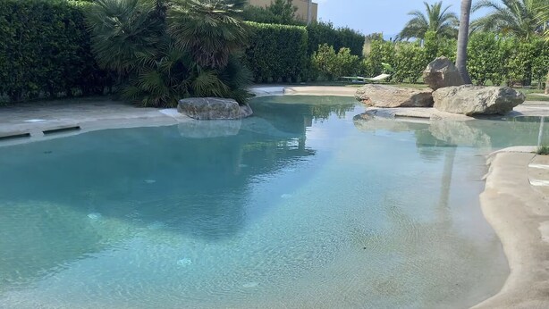 A clear swimming pool with a pebble bottom, surrounded by a landscaped area with rocks and greenery. - Located in a quiet and pleasant setting a stone's throw from the sea (Toscana)