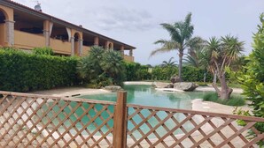 A pool area with a wooden fence, palm trees, and a building with a tiled roof. - Located in a quiet and pleasant setting a stone's throw from the sea (Toscana)