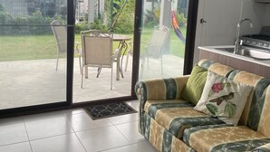 A living room with a sofa, a dining table with chairs, a sliding glass door leading to a patio, and a kitchen area with a stove.