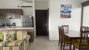 A modern kitchen with a built-in stove, refrigerator, and coffee maker. There is a dining area with a wooden table and chairs, and a sofa with patterned cushions.