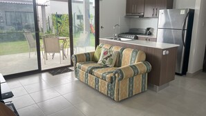 A compact living space with a sofa, a small kitchen area, and a sliding glass door leading to an outdoor patio.