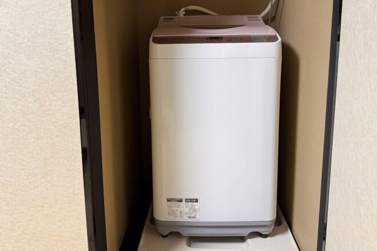 A white, compact, wall-mounted device, likely a heater or air conditioner, in a corner with a beige wall and a black frame.
