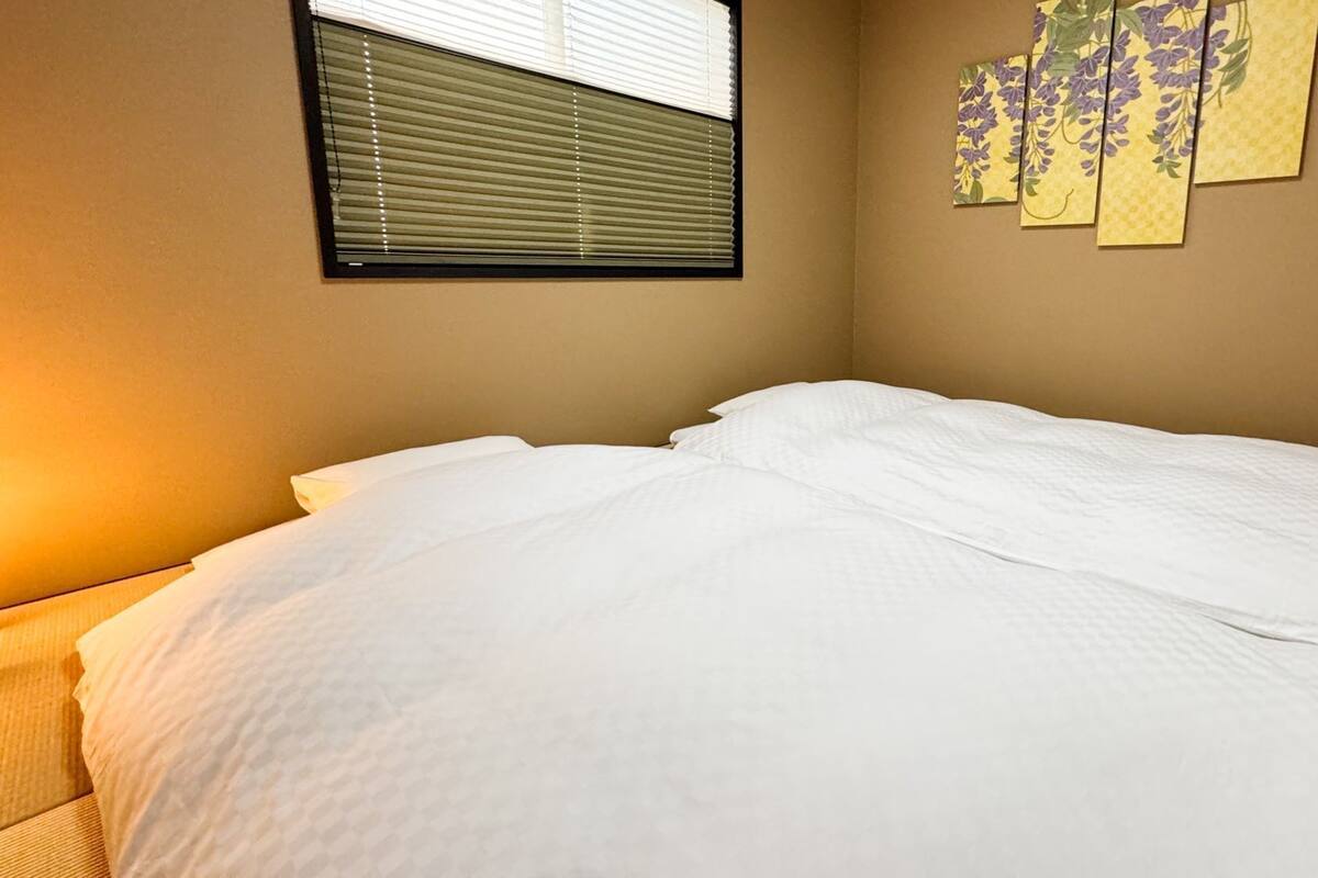 A neatly made bed in a room with a window and a wall-mounted artwork.