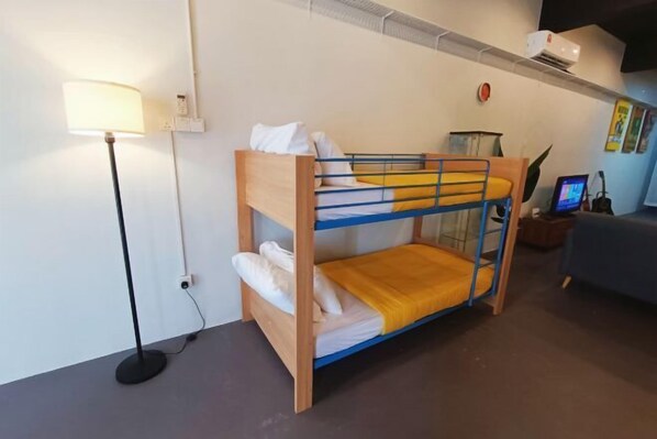 A bunk bed with a desk and lamp, a sofa, and a wall-mounted air conditioner.