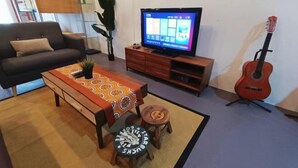 Sala de estar com sofá, mesa de centro, televisão e um violão.