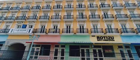 Un immeuble à plusieurs étages doté de balcons, de devantures de magasins et d’une enseigne pour le restaurant « ROTIZU ».