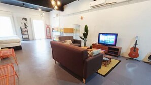 Uma sala moderna com sofá, TV, guitarra e um espaço de refeições com cadeiras.