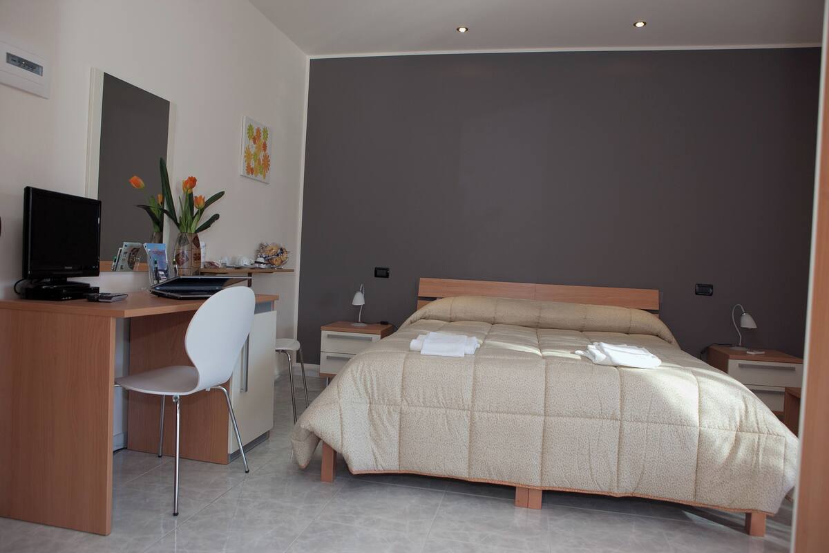 A modern hotel room with a bed, a desk, a chair, and a TV.